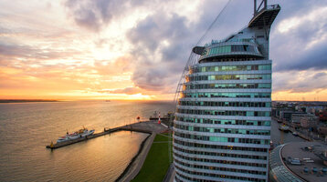ATLANTIC Hotel Sail City in Bremerhaven, bei Sonnenuntergang am Wasser, mit modernem, gebogenem Glasdesign.