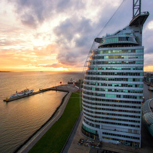 ATLANTIC Hotel Sail City – Exterior view ATLANTIC Hotel Sail City in Bremerhaven, at sunset on the waterfront, with modern, curved glass design.