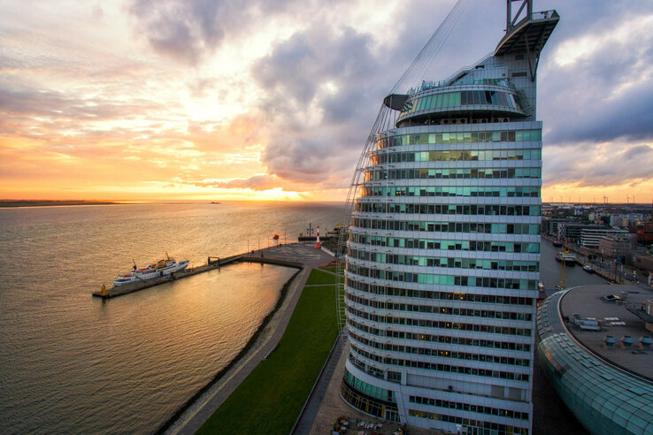 ATLANTIC Hotel Sail City in Bremerhaven, at sunset on the waterfront, with modern, curved glass design.