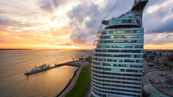 ATLANTIC Hotel Sail City in Bremerhaven, at sunset on the waterfront, with modern, curved glass design.