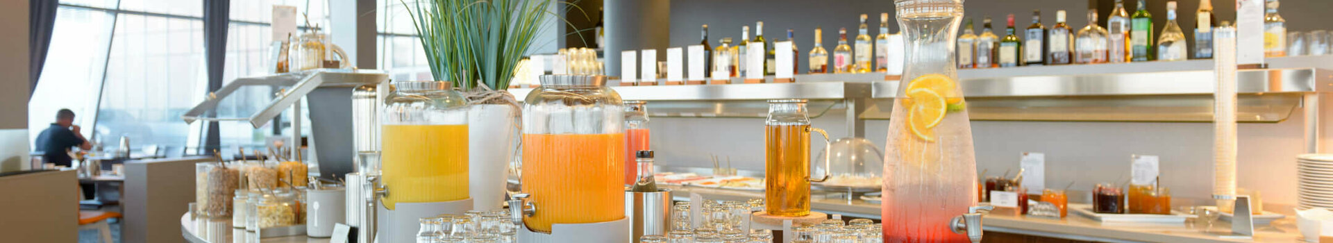 Breakfast in the Restaurant Strom | ATLANTIC Hotel Sail City Drinks bar in the ATLANTIC Hotel Sail City with juice dispensers and glasses, modern interior in the background.