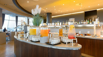 Frühstück im Restaurant Strom | ATLANTIC Hotel Sail City Getränkebar im ATLANTIC Hotel Sail City mit Saftspendern und Gläsern, modernes Interieur im Hintergrund.