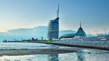 ATLANTIC Hotel Sail City - unique wedding location View of the ATLANTIC Hotel Sail City in Bremerhaven, on the shore with sand and sea at sunset.