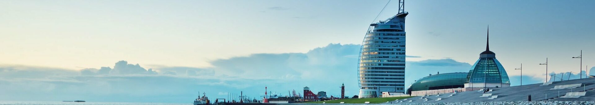 Blick auf das ATLANTIC Hotel Sail City in Bremerhaven, am Ufer mit Sand und Meer bei Sonnenuntergang.