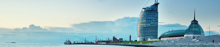Blick auf das ATLANTIC Hotel Sail City in Bremerhaven, am Ufer mit Sand und Meer bei Sonnenuntergang.