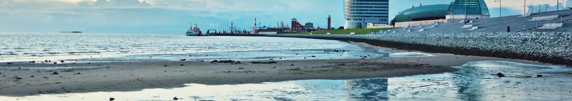 View of the ATLANTIC Hotel Sail City in Bremerhaven, on the shore with sand and sea at sunset.