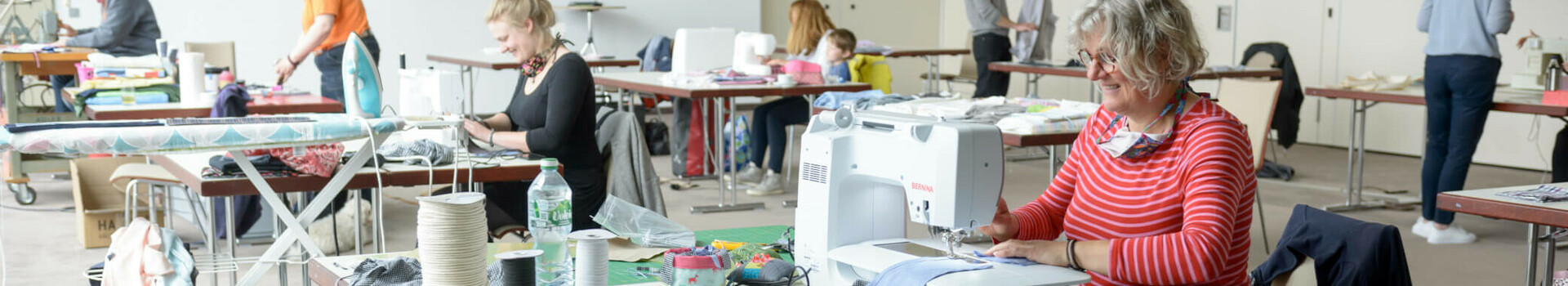 Personen nähen in hellem Raum des ATLANTIC Hotel Sail City Bremerhaven. Nähmaschinen und Stoffe auf Tischen.