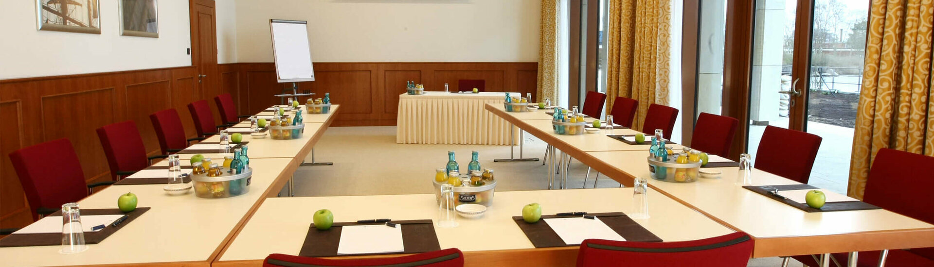 Function room for meetings and conferences Bright conference room with U-shaped table arrangement, red chairs and daylight, equipped for meetings.