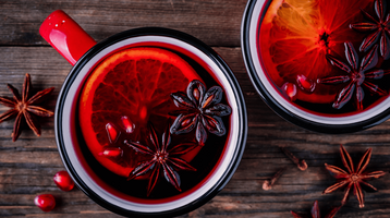 Zwei Becher mit rotem Glühwein und einer Orangenscheibe