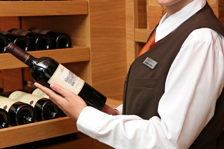 Hotelmitarbeiterin hält eine Weinflasche vor einem Regal mit weiteren Flaschen im ATLANTIC Hotel Kiel.