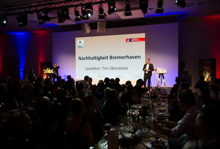 Ein Redner spricht auf einer Bühne über Nachhaltigkeit in Bremerhaven vor einem Publikum im ATLANTIC Hotel Sail City.