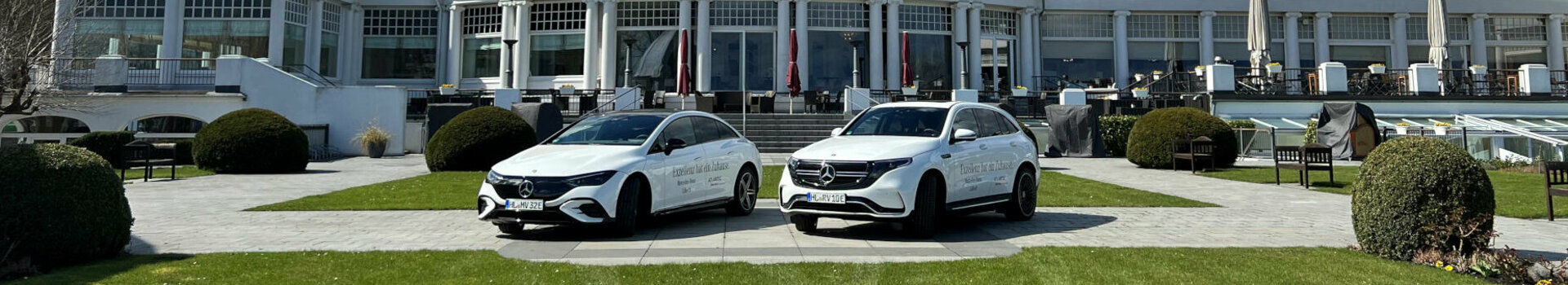 ATLANTIC Grand Hotel Travemünde mit rotem Dach, davor zwei weiße Autos und gepflegter Rasen unter blauem Himmel.