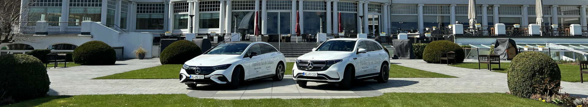 ATLANTIC Grand Hotel Travemünde with a red roof, two white cars in front and a well-tended lawn under a blue sky.