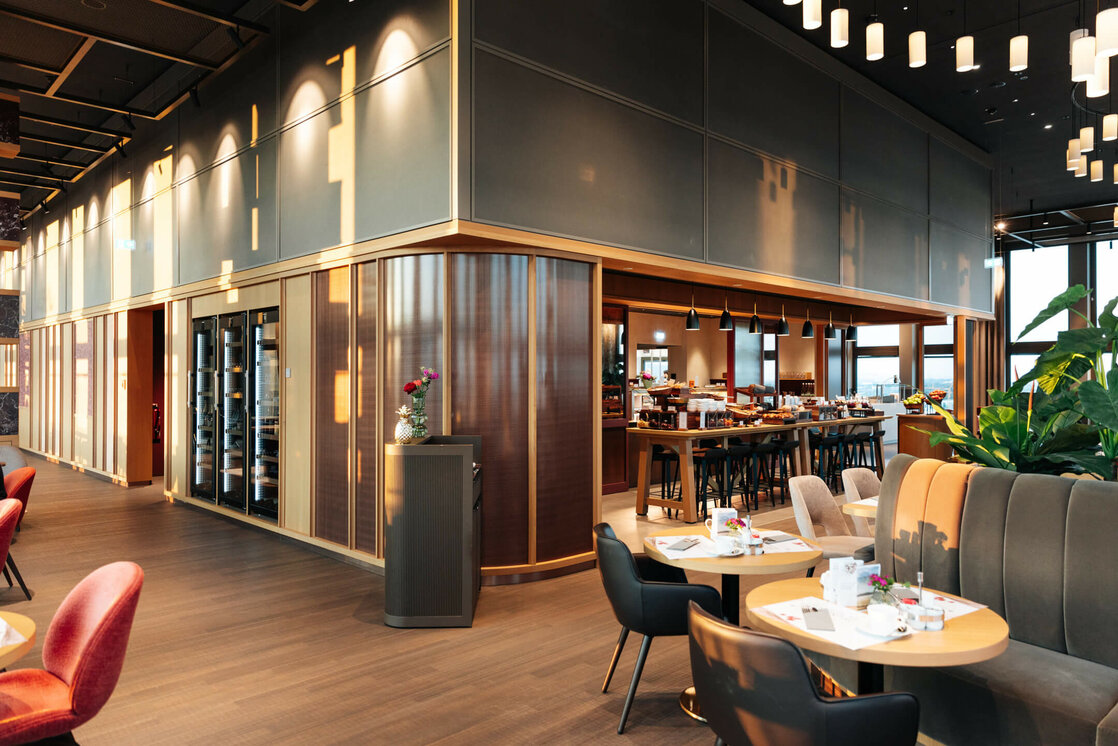 ATLANTIC Hotel Heidelberg Breakfast Modern hotel restaurant with stylish furnishings, wooden tables, cozy seating areas and decorative plants.