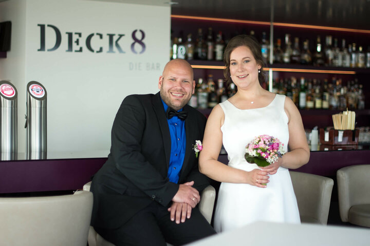 Couple in festive attire in the Bar Deck 8 of the ATLANTIC Hotel Kiel, surrounded by drinks and decorations.