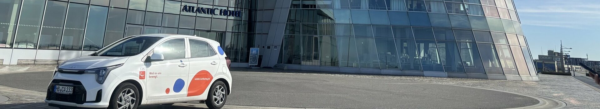 Ein weißer Kia Rio mit cambio-Logo steht vor dem ATLANTIC Hotel Sail City