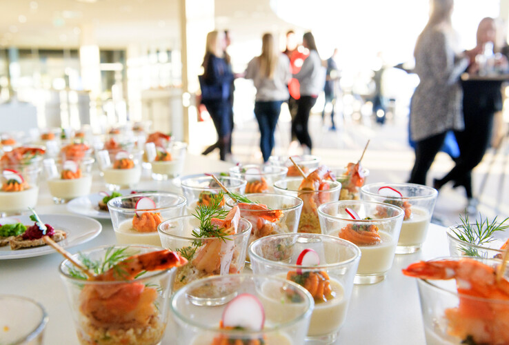 Gläser mit Garnelen und Vorspeisen auf einem Tisch im ATLANTIC Hotel Sail City, unscharfe Personen im Hintergrund.