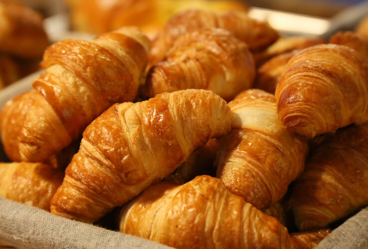 Fresh croissants in a basket, baked golden brown, ideal for a hotel breakfast buffet.