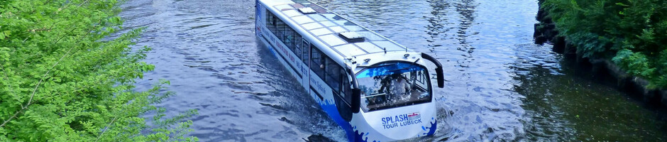 Amphibienbus auf Fluss vor historischer Altstadt Lübeck, mit Kirchtürmen im Hintergrund.