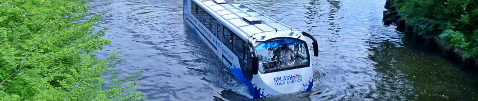 Amphibious bus on river in front of historic old town Lübeck, with church towers in the background.