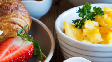 Nahaufnahme eines Frühstückstisches mit Früchten, Brötchen, Croissant, Rührei und Aufstrichen