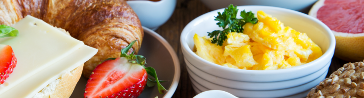 Nahaufnahme eines Frühstückstisches mit Früchten, Brötchen, Croissant, Rührei und Aufstrichen