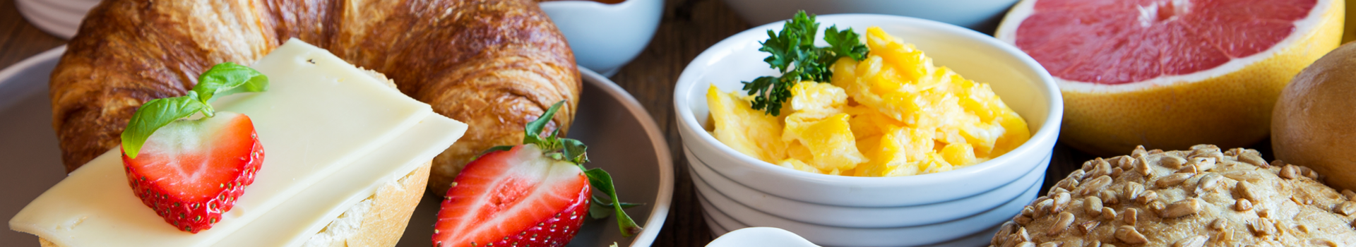 Nahaufnahme eines Frühstückstisches mit Früchten, Brötchen, Croissant, Rührei und Aufstrichen