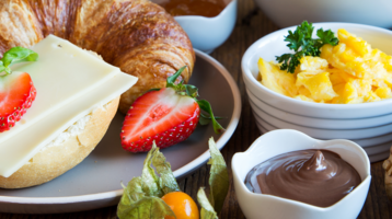 Nahaufnahme eines Frühstückstisches mit Früchten, Brötchen, Croissant, Rührei und Aufstrichen