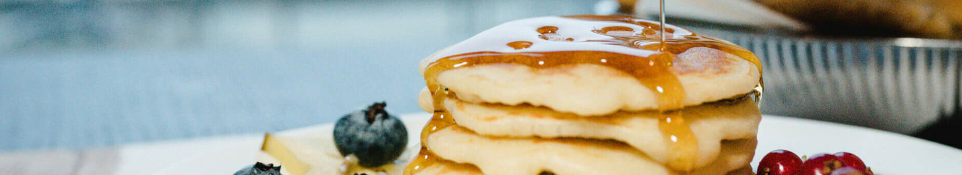 A stack of pancakes with berries and syrup on a plate, a blurred table in the background.