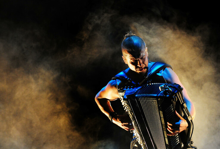 Ein Musiker spielt Akkordeon in dramatischer Beleuchtung und Nebel auf einer Bühne.