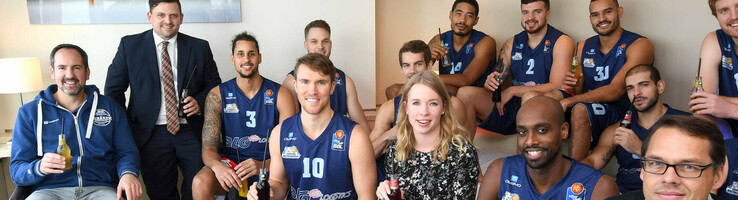 ATLANTIC Hotelgruppe bleibt Team Partner der Eisbären Bremerhaven Eine Gruppe von Menschen, darunter Basketballspieler in Trikots, sitzt in einem modernen Hotelzimmer.