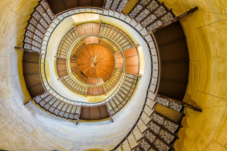 Blick von unten auf eine kunstvolle Wendeltreppe im ATLANTIC Grand Hotel Travemünde, mit verzierten Geländern.