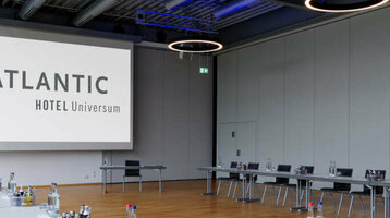 Moderner Konferenzraum im ATLANTIC Hotel Universum mit U-förmiger Tischanordnung und großen Fenstern.