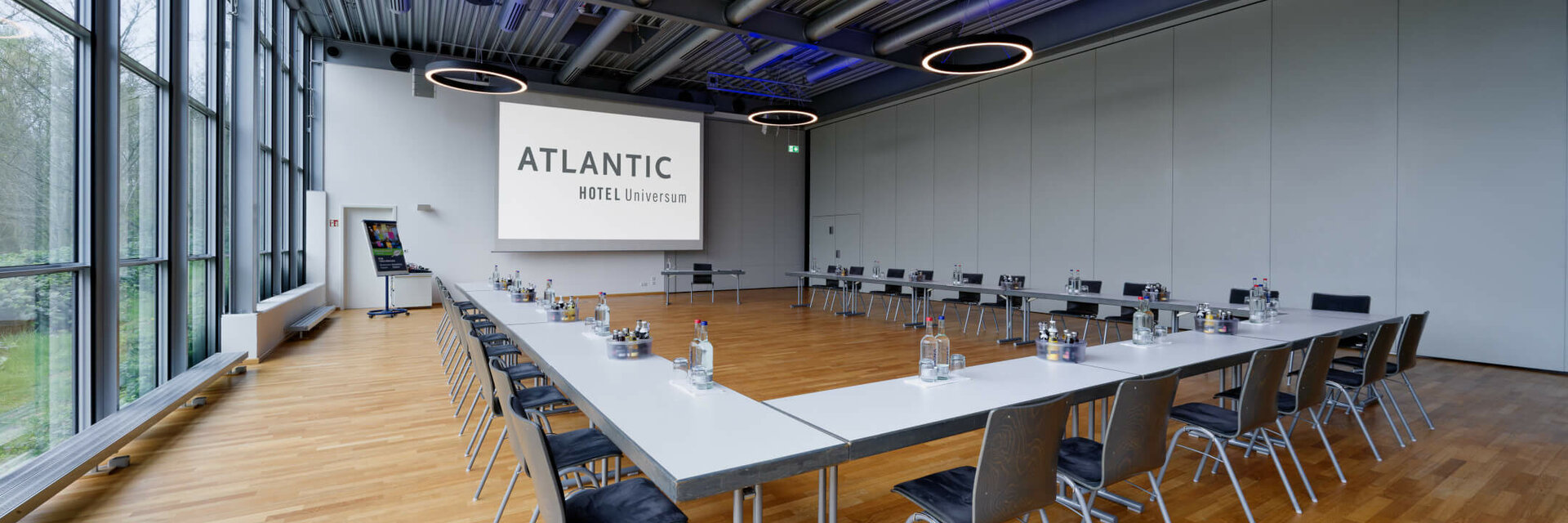 Moderner Konferenzraum im ATLANTIC Hotel Universum mit U-förmiger Tischanordnung und großen Fenstern.