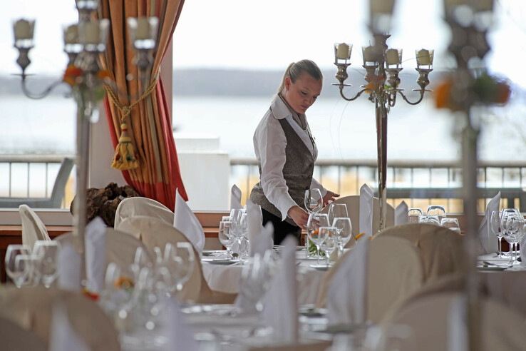 Restaurant im ATLANTIC Grand Hotel Travemünde: Eine Servicemitarbeiterin deckt elegant eingedeckte Tische ein.