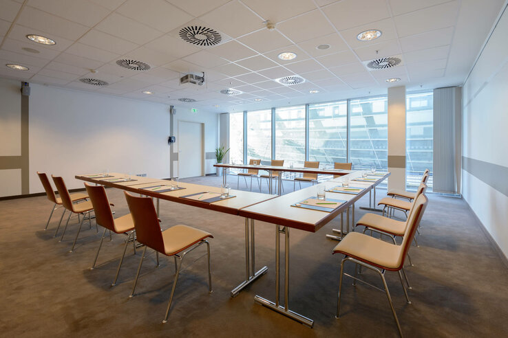 Modern conference room with U-shaped seating, daylight through large windows, in the ATLANTIC Hotel Sail City Bremerhaven.