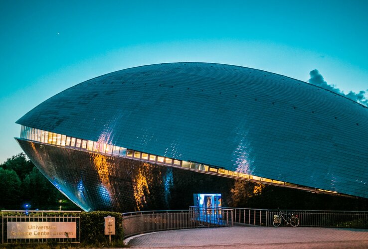 Futuristisches Gebäude des Universum Bremen bei Dämmerung, mit leuchtenden Fenstern und spiegelnder Fassade.