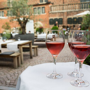 Kühle Drinks im Hofgarten des ATLANTIC Grand Hotel Bremen genießen Drei Gläser Rotwein auf einem Tablett im Außenbereich des ATLANTIC Grand Hotel Bremen, mit Tischen im Hintergrund.