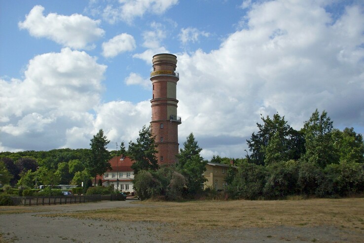 Roter Leuchtturm umgeben von Bäumen und Wolkenhimmel in Travemünde.