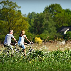 Fahrradverleih im ATLANTIC Hotel Landgut Horn Ein Paar fährt Fahrrad durch eine grüne Wiese vor einem Haus im Hintergrund.