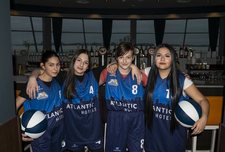 Four young basketball players in blue jerseys pose smiling in a hotel bar.