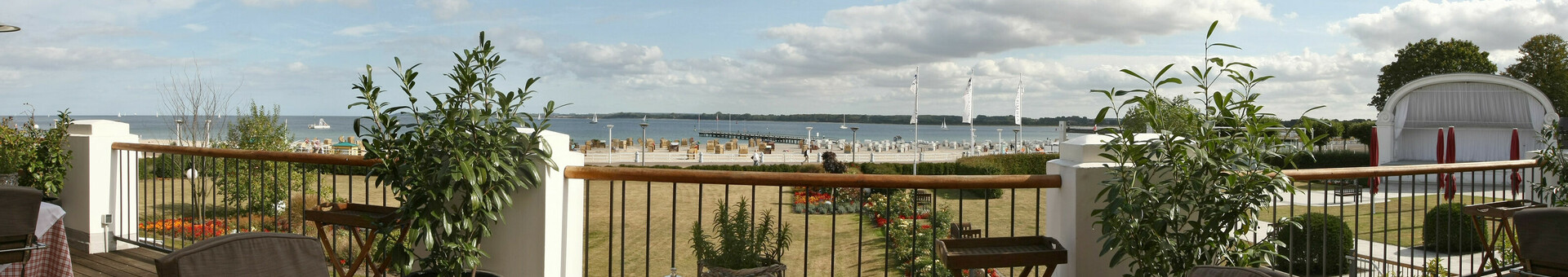Terrace with set table, view of the beach and sea, surrounded by plants, at the ATLANTIC Grand Hotel Travemünde.