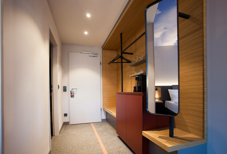 Modern hotel room hallway with wooden details, mirror, clothes rail, wardrobe and view into the bedroom at the ATLANTIC Hotel Airport.