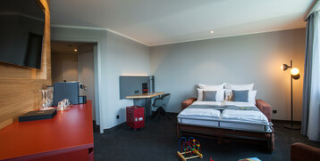 Modernes Hotelzimmer mit Doppelbett, Schreibtisch, Spielzeug auf dem Boden und gemütlicher Beleuchtung.