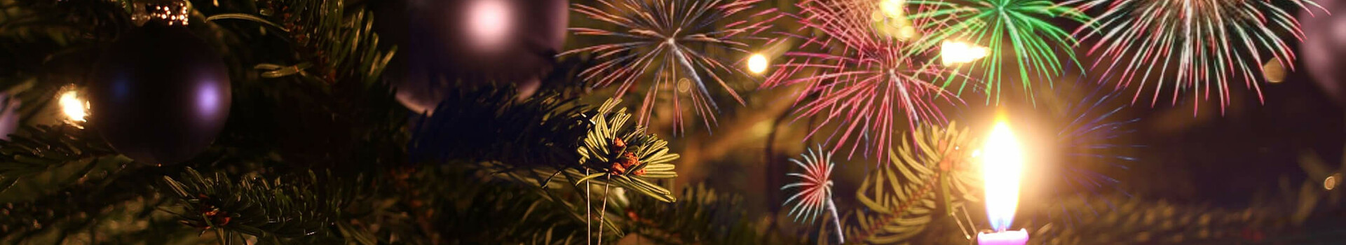 Weihnachtsbaum mit Kugeln und Kerze, bunte Feuerwerke im Hintergrund. Festliche Atmosphäre im ATLANTIC Grand Hotel Travemünde.