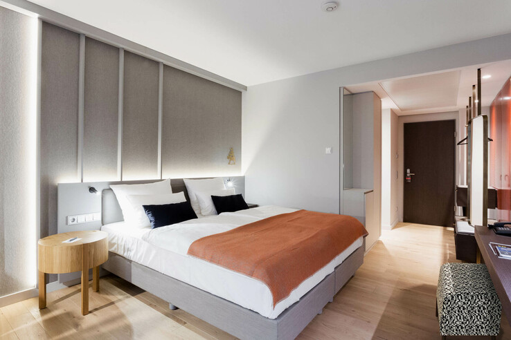 Modern hotel room with double bed, orange ceiling, bedside table and stylish interior at the ATLANTIC Grand Hotel Bremen.