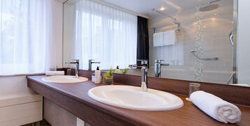 Modernes Hotelbad mit Doppelwaschbecken, Spiegelwand, Dusche, weißen Handtüchern und Pflanzenakzent.