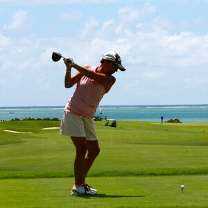 Golferin beim Abschlag auf einem grünen Golfplatz mit Meerblick im Hintergrund.