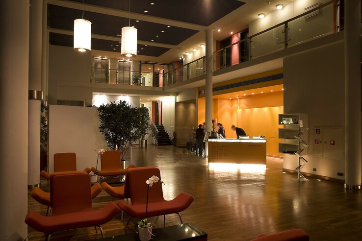 Moderne Hotel-Lobby mit orangefarbenem Empfangstresen, Sitzbereich und Pflanzen im ATLANTIC Hotel Universum Bremen.