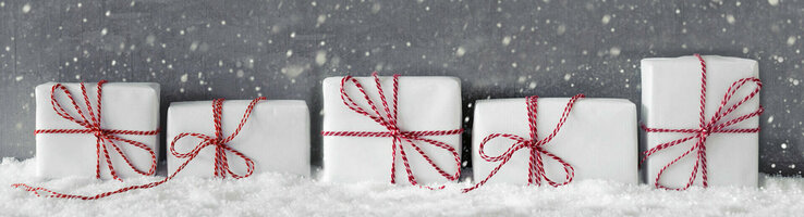 Weiße Geschenke mit roten Schleifen im Schnee vor grauem Hintergrund mit fallenden Schneeflocken.